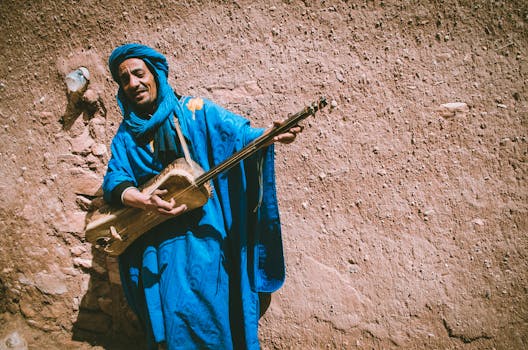 A Moroccan musician in vibrant blue plays a traditional instrument against a rustic wall.