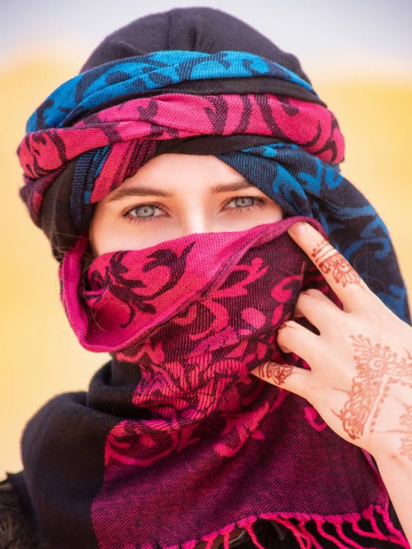 Discover Morocco 3 Days Marrakech To Fes Magic 7 A woman in Merzouga, Morocco, wearing a colorful hijab and henna tattoo, standing in the desert.
