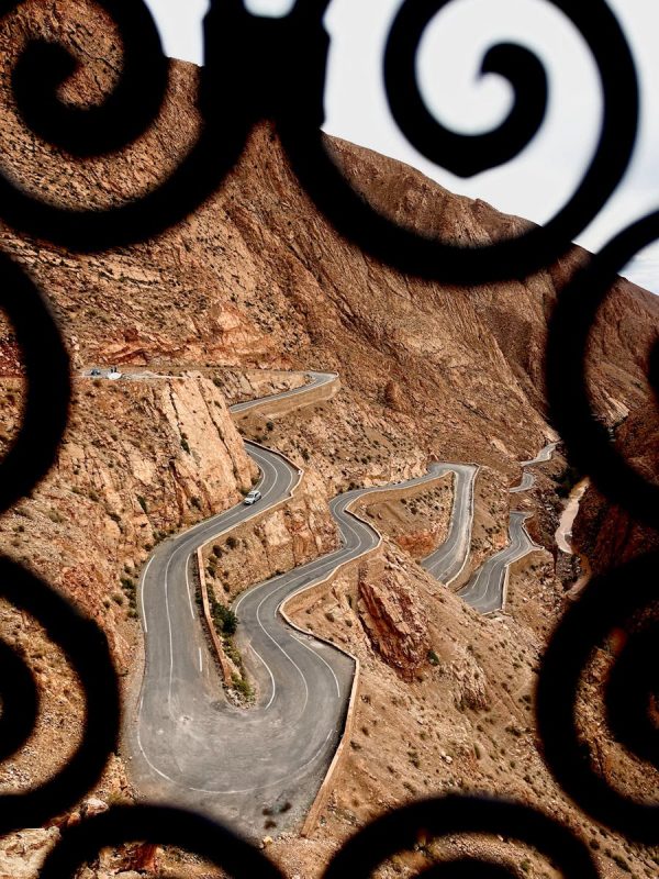 Discover Morocco 3 Days Marrakech To Fes Magic 3 Scenic view of a winding road through the Atlas Mountains framed by ornate ironwork.