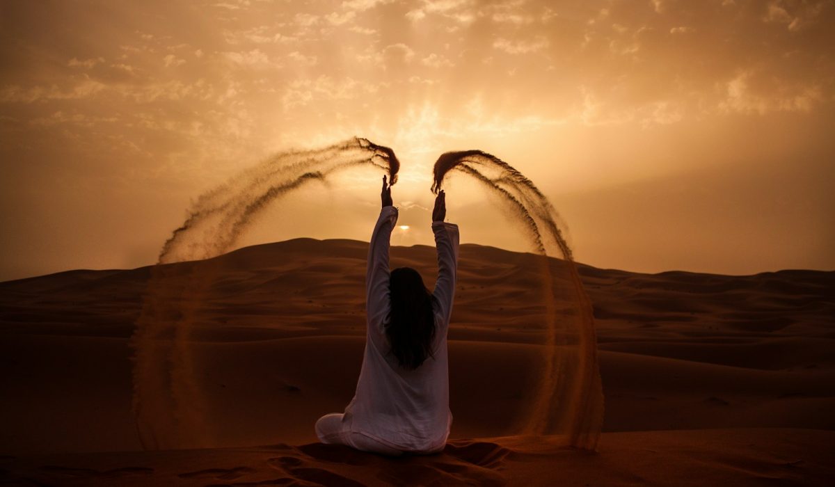 woman sitting on desert while playing sand during golden hour